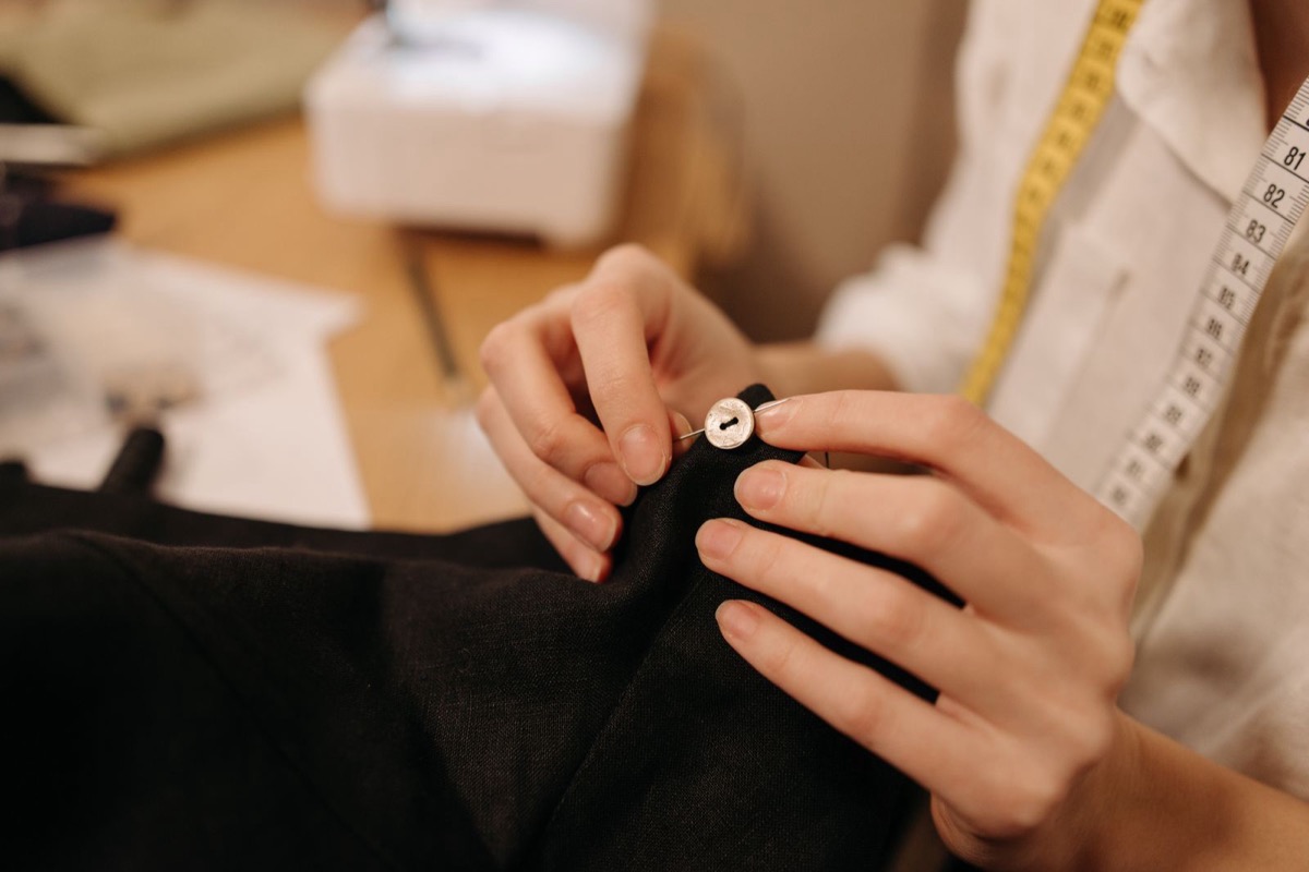 Hands hand-sewing a button onto dark fabric with needle and thread